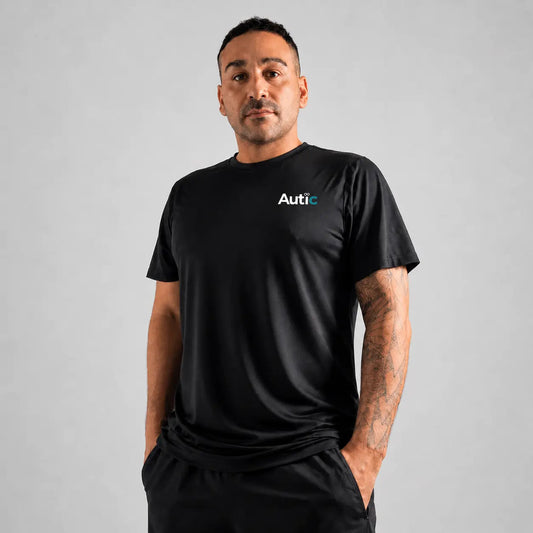 Man wearing a black Autic sensory friendly bamboo T shirt with a small chest logo against a light grey background.